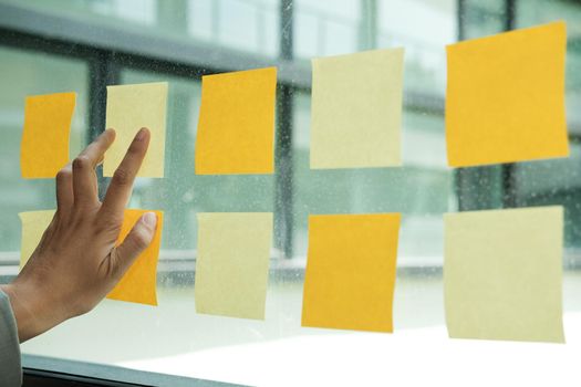 hand touch on adhesive notes on glass wall at workplace. Sticky note paper reminder schedule for creative idea & business brainstorming