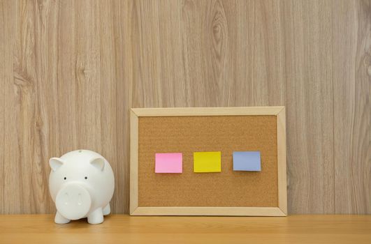 sticky notes paper reminder on cork board & piggy bank on wooden desk. money saving finance investment concept