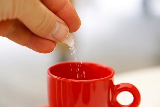 hand putting sugar in a cup of coffee or tea. Close up