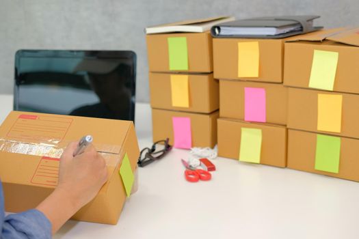 startup small business owner writing address on cardboard box at workplace. freelance woman entrepreneur seller prepare parcel box for delivery product to customer.  Online selling, e-commerce concept