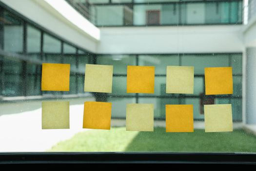 adhesive notes on glass wall at workplace. Sticky note paper reminder schedule for discussing creative idea & business brainstorming