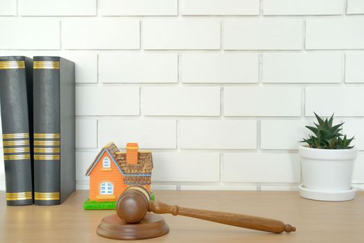 judge gavel law book & home house model on wooden desk near white brick wall. real estate dispute & property auction concept