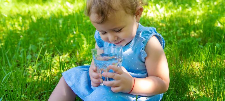 The child drinks water from a glass. Selective focus. Kid.