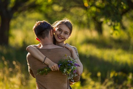 young couple hugging in nature, girl holding flowers