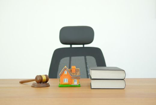 judge gavel law book & home house model on wooden desk near white brick wall. real estate dispute & property auction concept