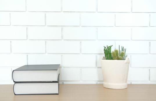book on wooden desk table near white brick wall. office workplace top view. education concept. succulent cactus plant in pot