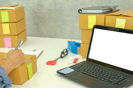 startup small business owner writing address on cardboard box at workplace. freelance woman entrepreneur seller prepare parcel box for delivery product to customer.  Online selling, e-commerce concept