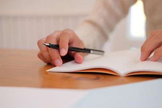 man wearing cream sweater writing note on notebook at home