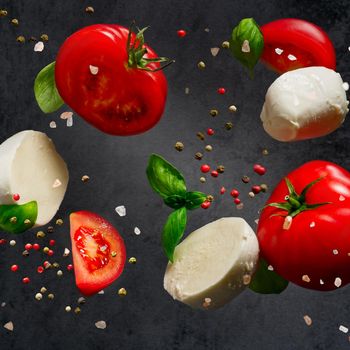 Falling caprese salad ingredients on dark background. Falling mozzarella cheese and tomatoes on dark background