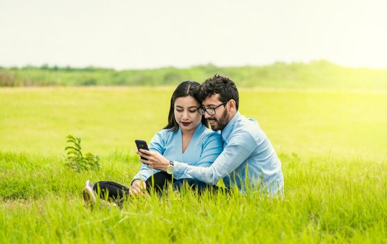 Young couple in love taking a selfie in the field, Two lovers sitting on the grass taking selfies, People in love taking selfies in the field with their smartphone