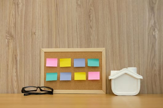 sticky notes paper reminder on cork board & house model on wooden desk. real estate investment. property buying mortgage loan