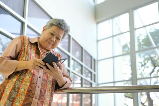 asian elder woman holding mobile phone on terrace. elderly female using smartphone on patio. senior texting message with cellphone