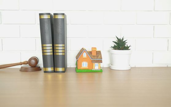 judge gavel law book & home house model on wooden desk near white brick wall. real estate dispute & property auction concept