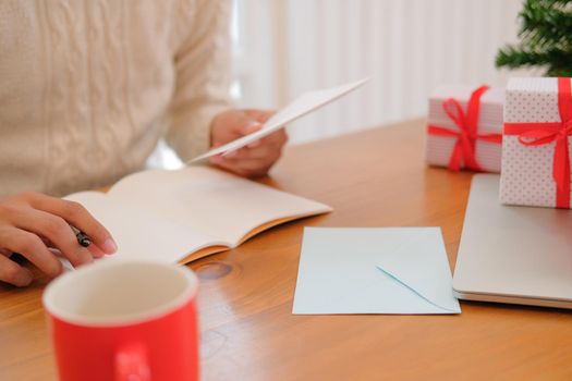 man wearing cream sweater writing christmas letter greeting card holiday wishes with xmas decoration.