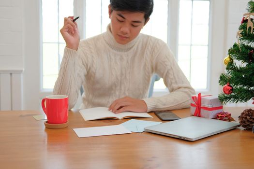 man wearing cream sweater writing note on notebook at home during christmas new year holiday celebration.