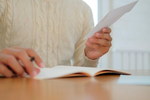 man wearing cream sweater writing christmas letter greeting card holiday wishes. xmas celebration.