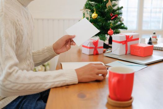 man wearing cream sweater writing christmas letter greeting card holiday wishes with xmas decoration.