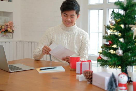 man wearing cream sweater opening sending christmas letter greeting card holiday wishes with xmas decoration