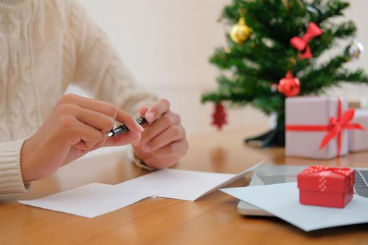 man wearing cream sweater thinking writing christmas letter greeting card holiday wishes with xmas decoration.