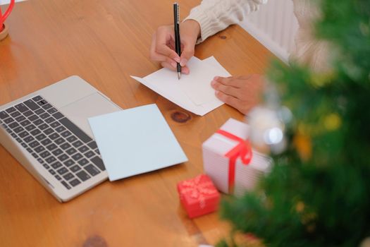 man wearing cream sweater writing christmas letter greeting card holiday wishes with xmas decoration.