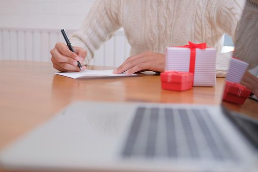 man wearing cream sweater writing christmas letter greeting card holiday wishes with xmas decoration.