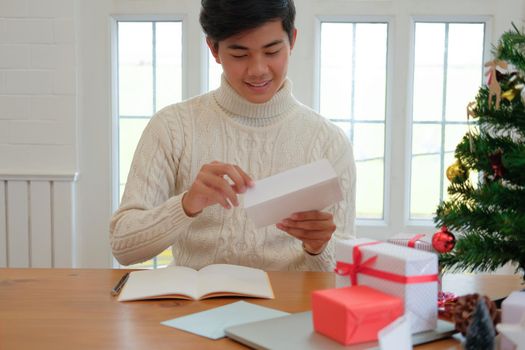 man wearing cream sweater opening sending christmas letter greeting card holiday wishes with xmas decoration