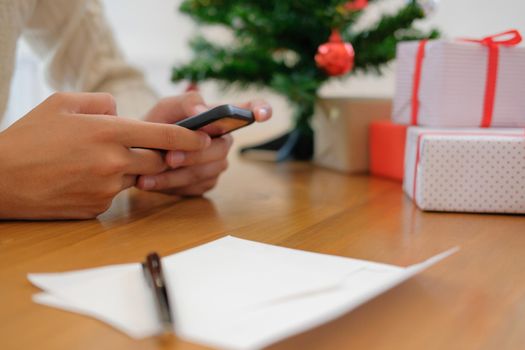man wearing cream sweater using mobile smart phone with christmas decoration. xmas new year holiday celebration.