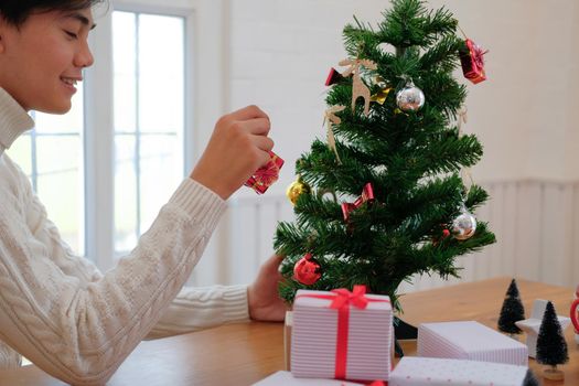 man wearing cream sweater decorating christmas tree. xmas new year holiday celebration.