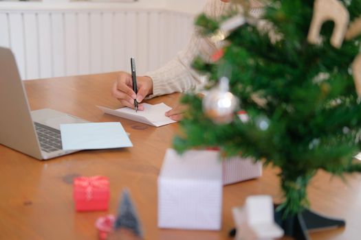 man wearing cream sweater writing christmas letter greeting card holiday wishes with xmas decoration.