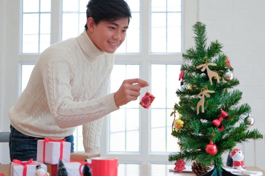 man wearing cream sweater decorating christmas tree. xmas new year holiday celebration.