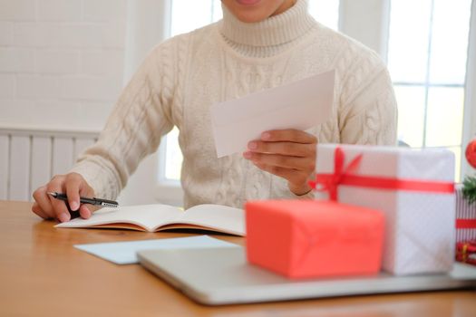 man wearing cream sweater writing christmas letter greeting card holiday wishes. xmas celebration.