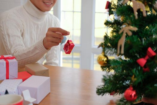 man wearing cream sweater decorating christmas tree. xmas new year holiday celebration.