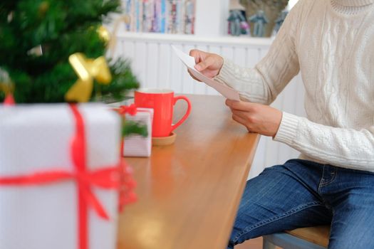 man wearing cream sweater opening sending christmas letter greeting card holiday wishes with xmas decoration