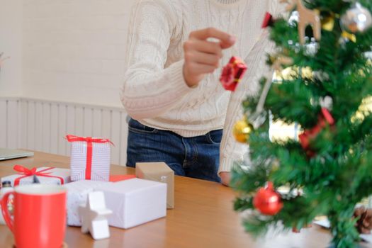 man wearing cream sweater decorating christmas tree. xmas new year holiday celebration.