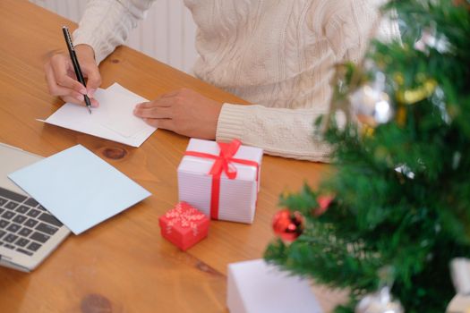 man wearing cream sweater writing christmas letter greeting card holiday wishes with xmas decoration.