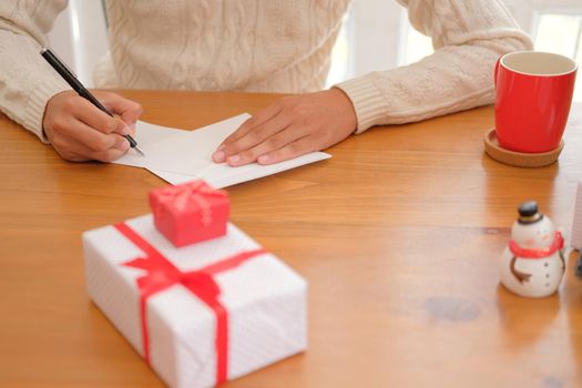 man wearing cream sweater writing christmas letter greeting card holiday wishes. xmas celebration.