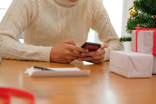 man wearing cream sweater using mobile smart phone with christmas decoration. xmas new year holiday celebration.