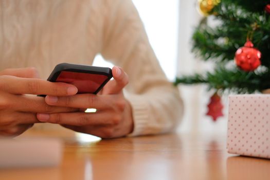 man wearing cream sweater using mobile smart phone with christmas decoration. xmas new year holiday celebration.