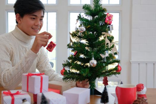 man wearing cream sweater decorating christmas tree. xmas new year holiday celebration.