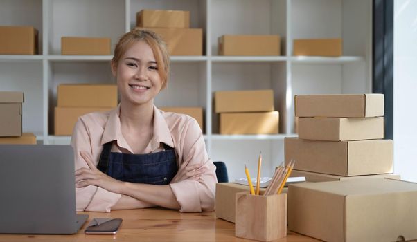 Young smiling beauty owner asian woman freelancer sme business online shopping working on laptop computer with parcel box at home - SME business online and delivery concept.