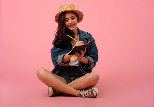 portrait of smiling young asian woman wearing jeans jacket writing note. studio shot