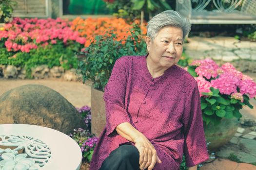 old elder woman resting in flower garden. asian elderly female relaxing in park. senior leisure lifestyle