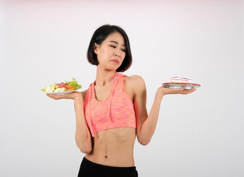 sporty fitness woman in sportswear with vegetable salad & cake on white background. healthy sport lifestyle