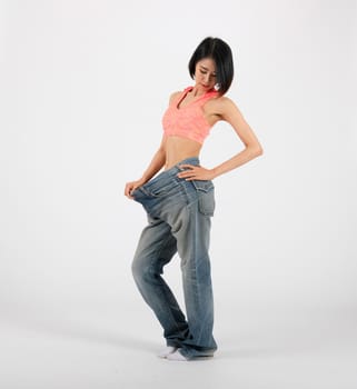 sporty fitness woman in loose jeans after losing weight on white background. healthy sport lifestyle