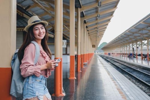 woman traveler holding camera taking photo at train station. travel trip journey concept