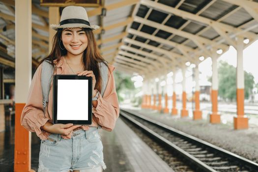 young woman traveler showing tablet with blank screen at train station. Travel journey trip concept