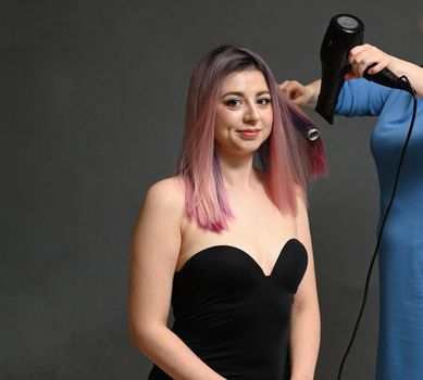 The hairdresser dries the dyed hair with a hairdryer of the model