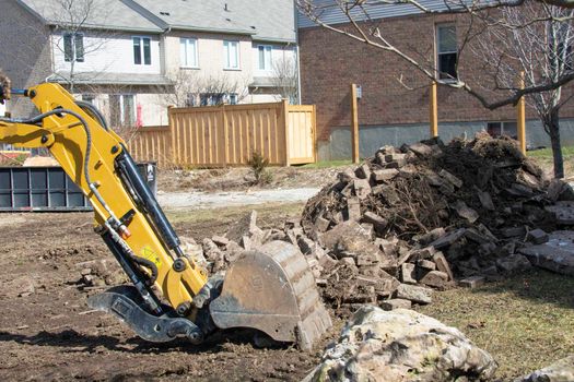 An excavator clears a site from debris and stones at a construction site for the construction of a cottage