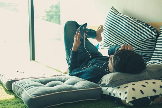 asian male teenager man listening to music from smart mobile phone while lying on floor at home