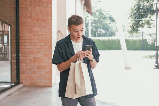 surprised man holding paper shopping bags & mobile smart phone. consumerism lifestyle
